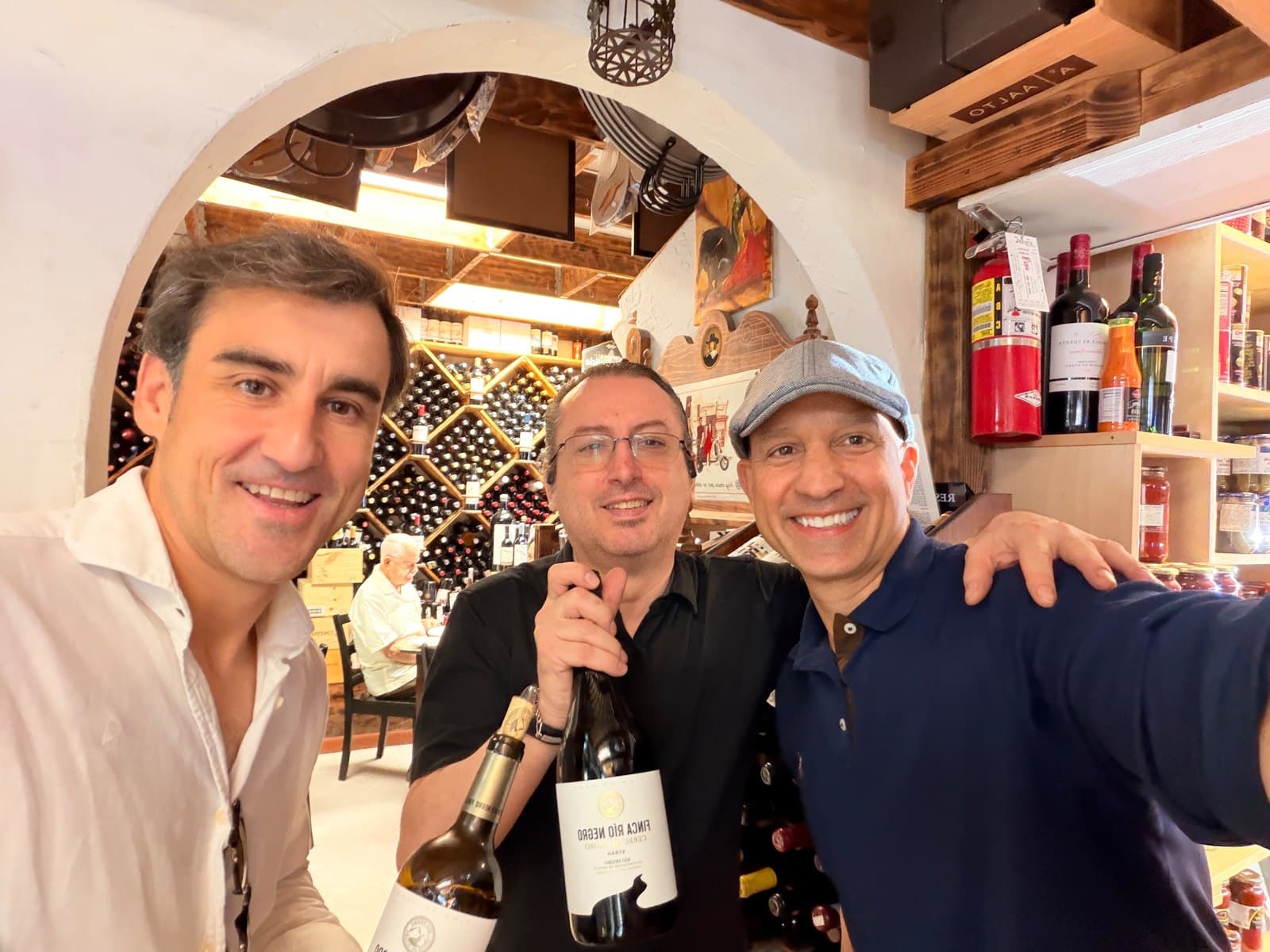 Three men with a bottle in front of a wine cellar