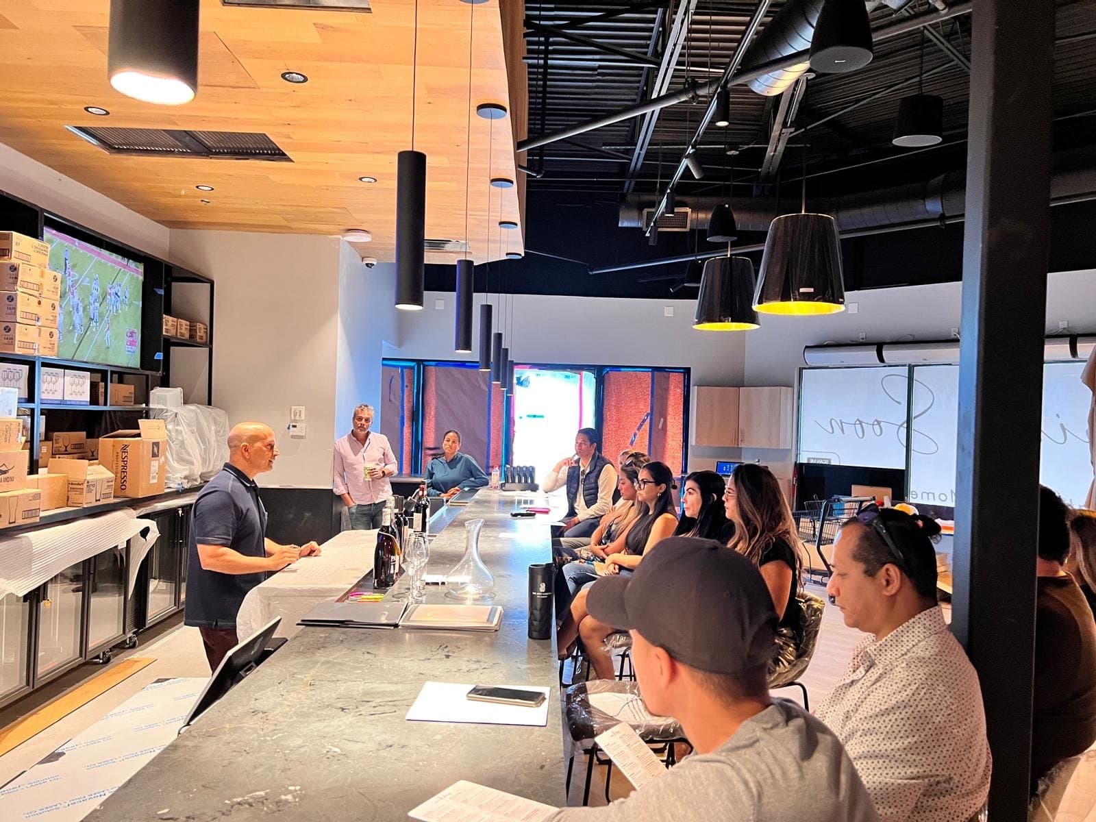 A long counter lined with seated guests facing a presenter, a map of the wine regions on the screen behind