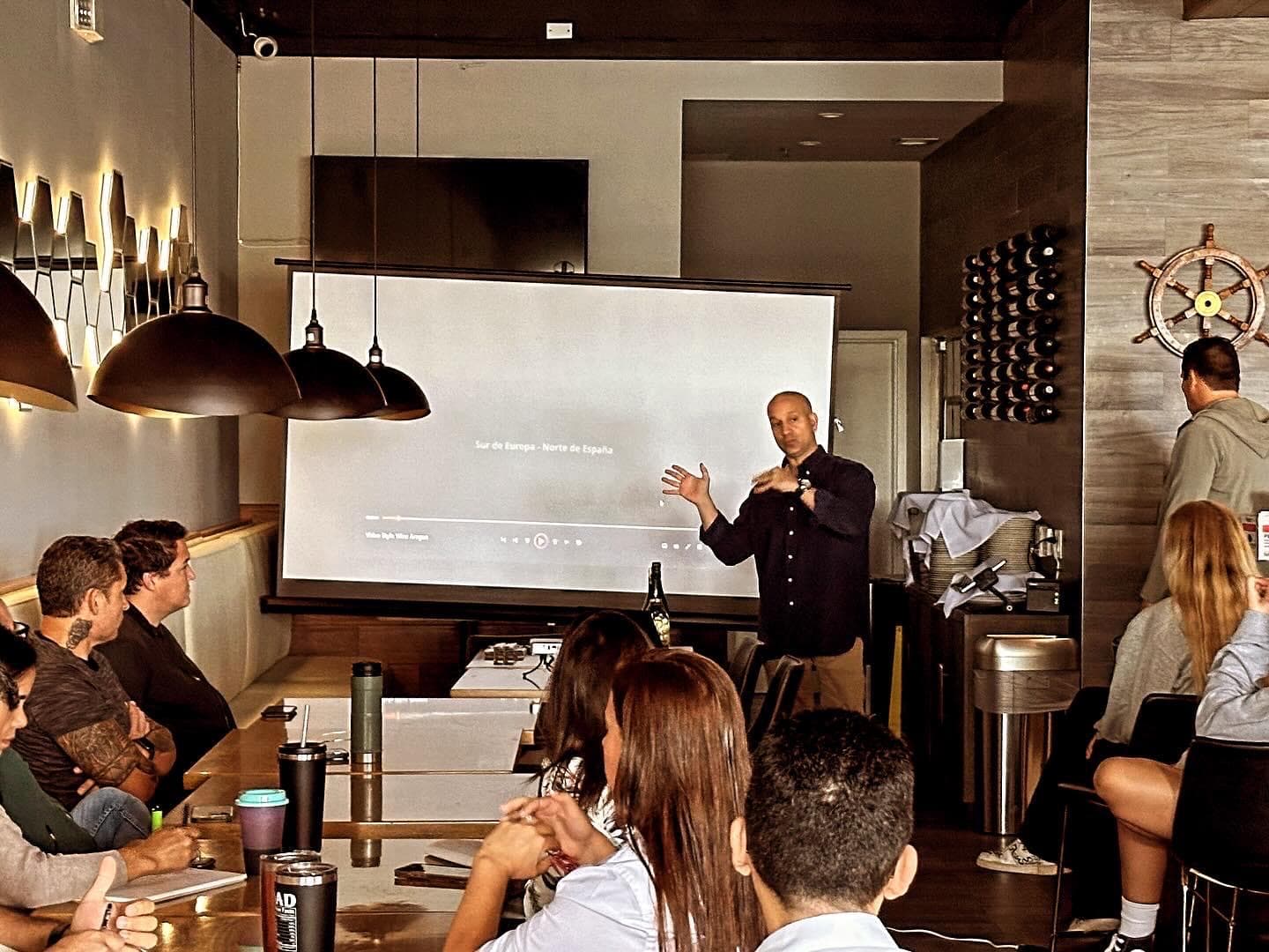 A seated class with glasses in front of them while an instructor presents at a screen