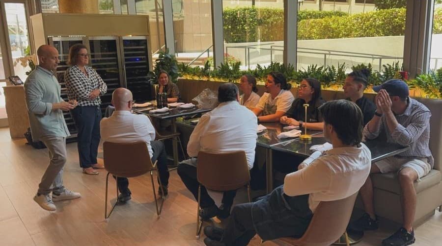 A presenter addressing a seated group around tables in a bright room