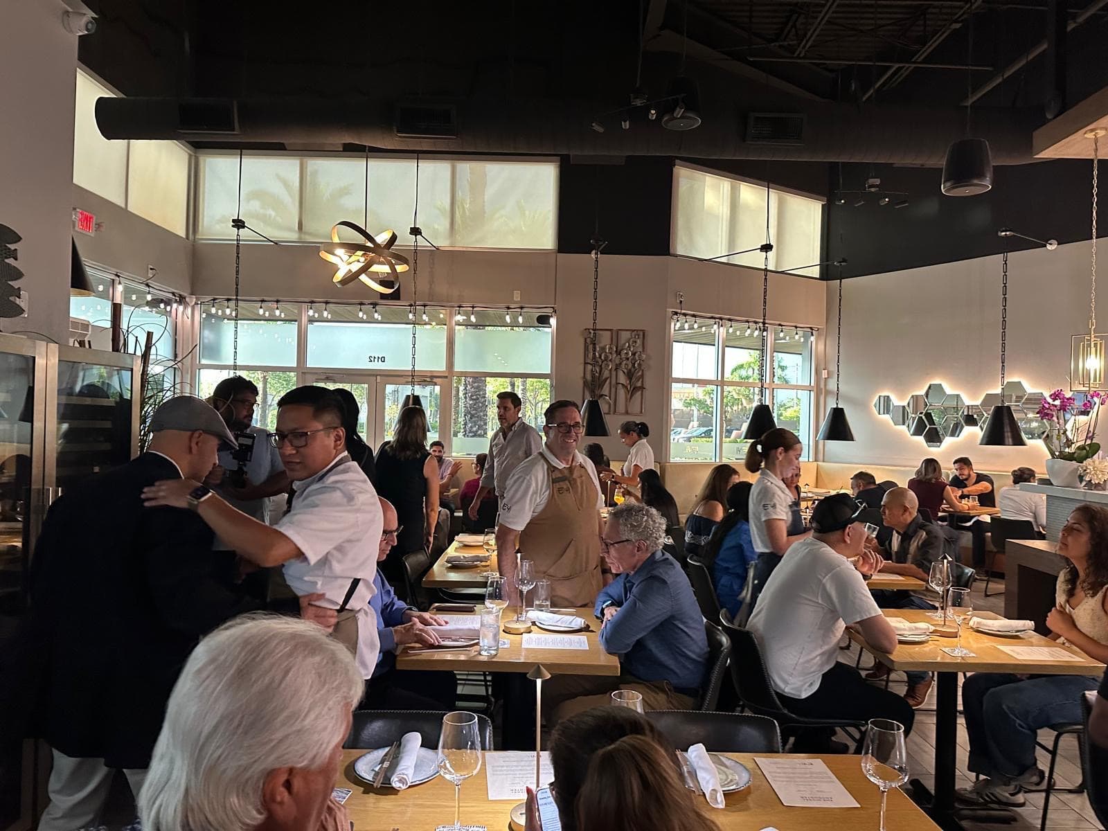 A full restaurant dining room of seated guests at a tasting, a presenter standing at one side