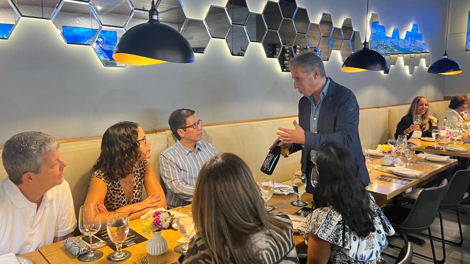 A host presenting a bottle to guests seated around a restaurant table