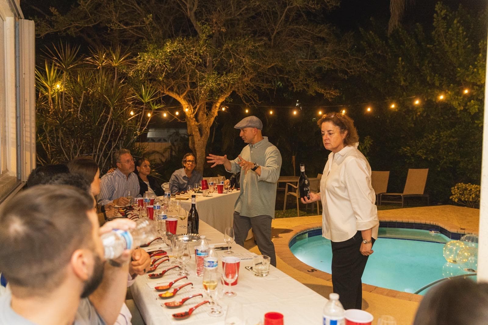 Guests standing along a long table of glassware in a bright room lined with wine racks