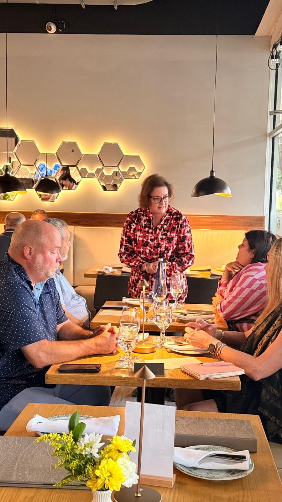 A host standing at a restaurant table talking to seated guests