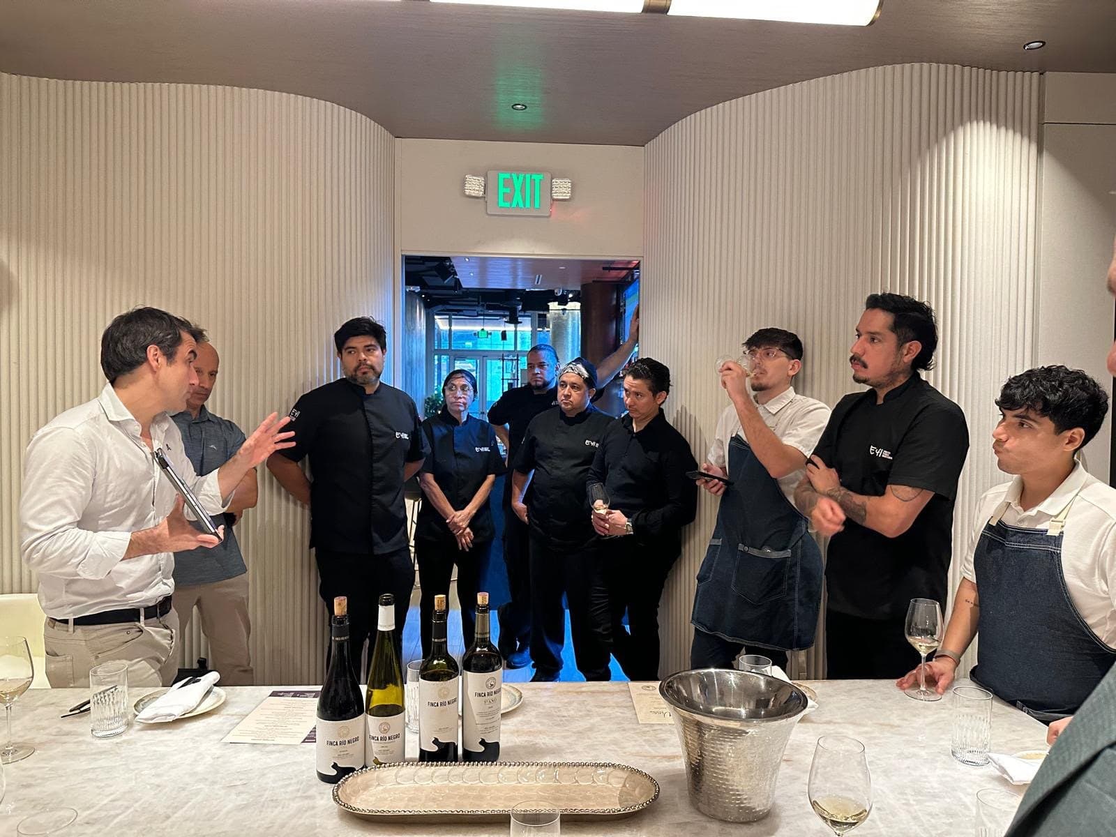 A restaurant team gathered along a wall while bottles and tasting mats wait on the counter