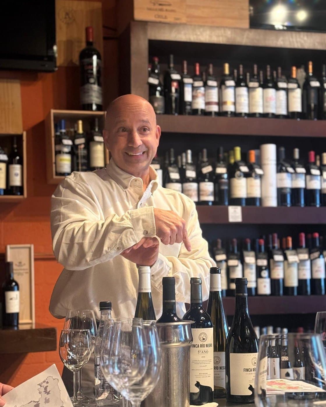 Gustavo Piteo opening a bottle behind the counter of a wine shop, Finca Río Negro bottles in front of him